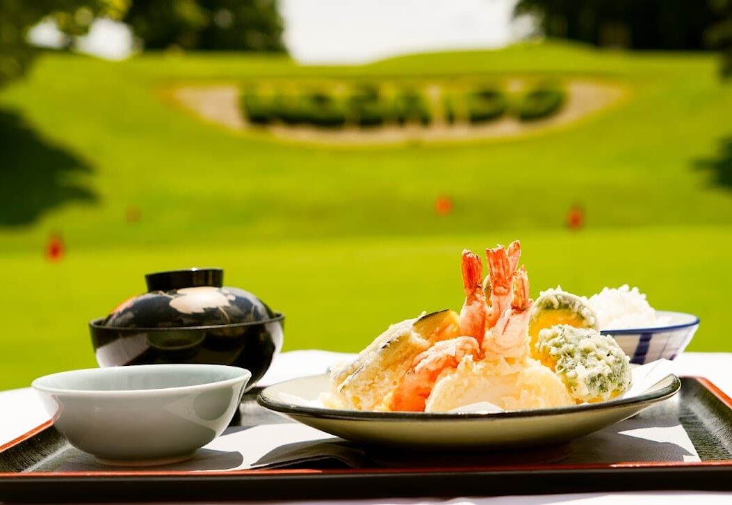 Nahaufnahme eines Tellers mit Tempura Garnelen. Im Hintergrund ist der Golfplatz zu sehen.